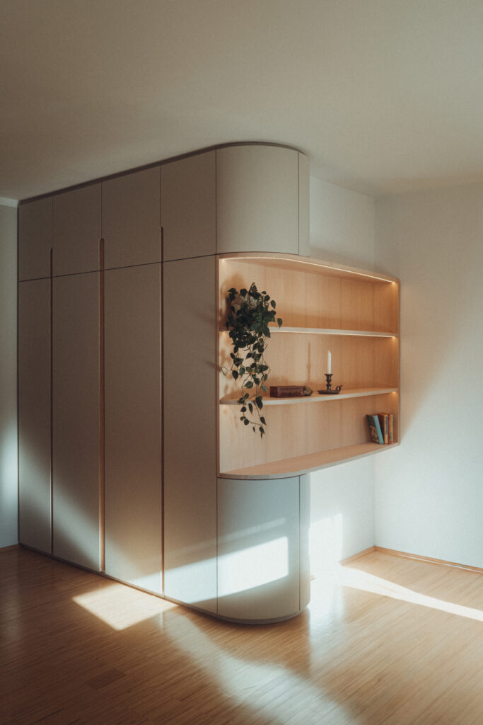 Eck-Einbauschrank nach Maß aus Esche und Linoleum mit warmer LED-Innenbeleuchtung.