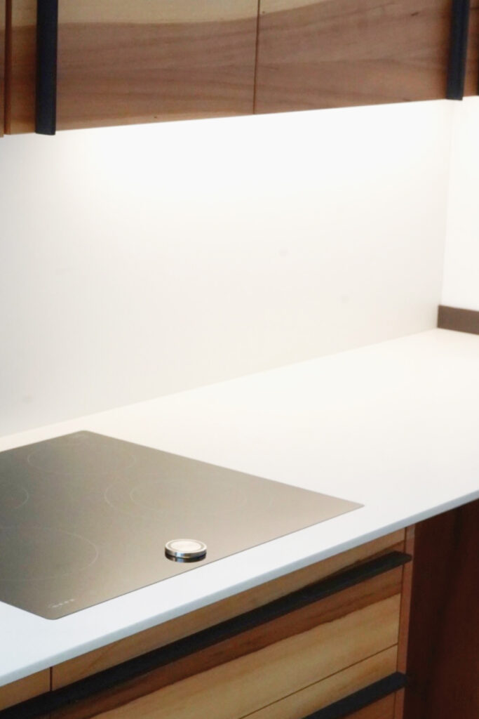 Großzügige Küche aus Apfelholz-Fronten mit einer Arbeitsplatte aus weißem Mineralwerkstoff.