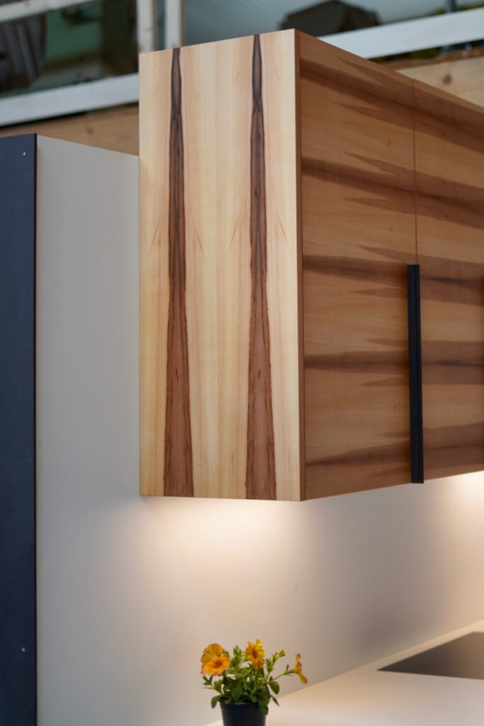 Großzügige Küche aus Apfelholz-Fronten mit einer Arbeitsplatte aus weißem Mineralwerkstoff.